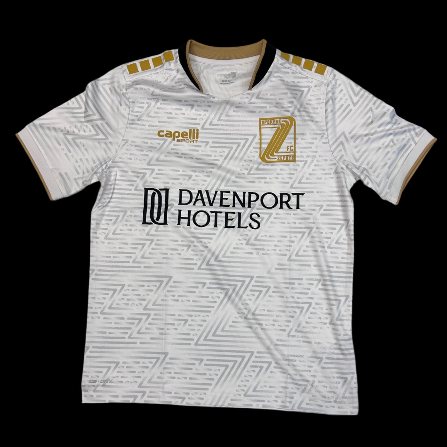 white soccer jersey with a silver repeated "Z" gradient pattern, a black Davenport Hotels logo, a gold Spokane Zephyr "Z" crest and a gold Capelli sport logo