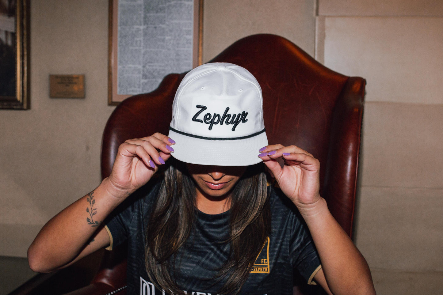 Aryssa Mahrt wearing a white cap with a black rope and black cursive 'Zephyr' logo in an indoor setting