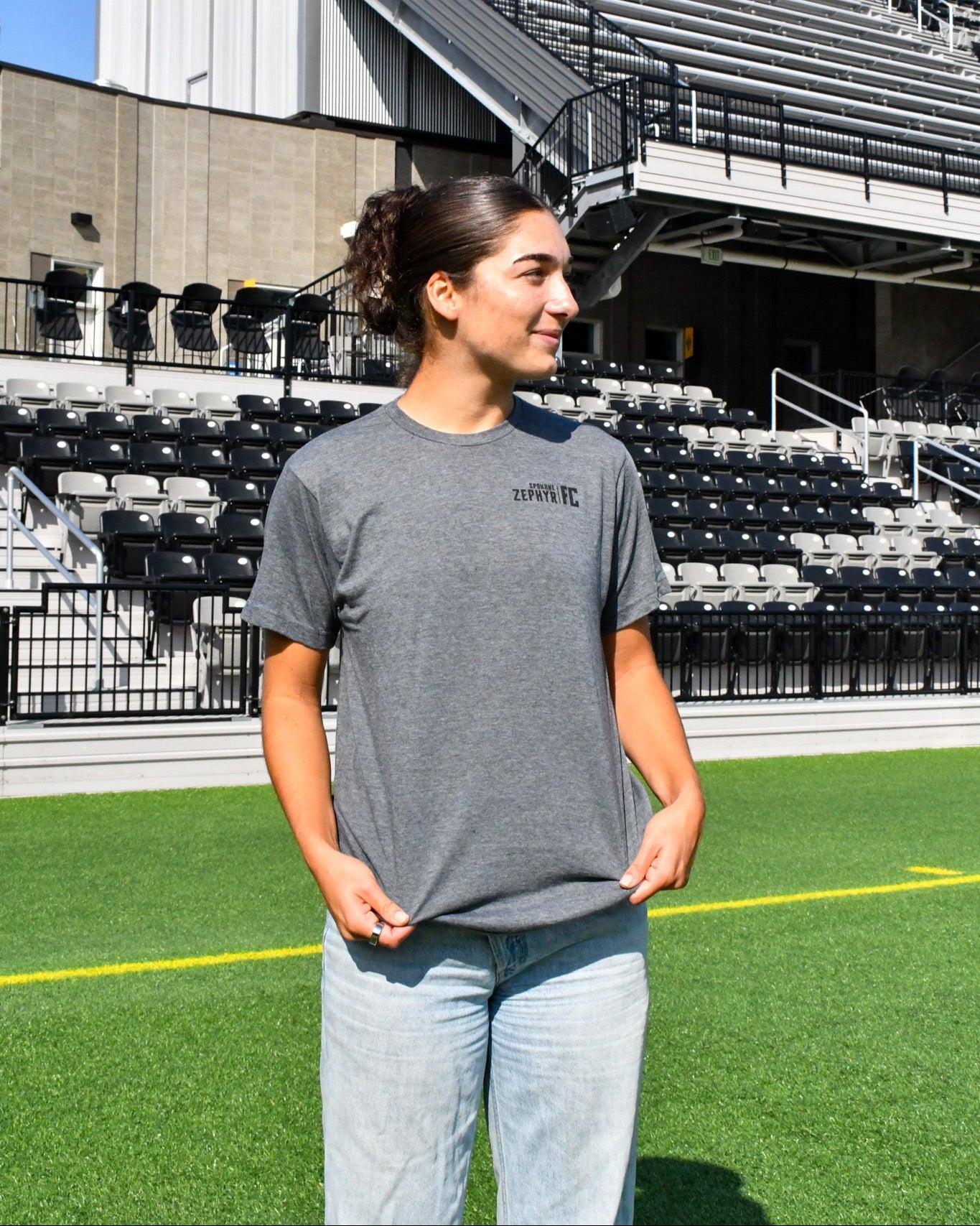 Lena Silano wearing a heathered gray t-shirt with a Spokane Zephyr FC Wordmark on a sports field