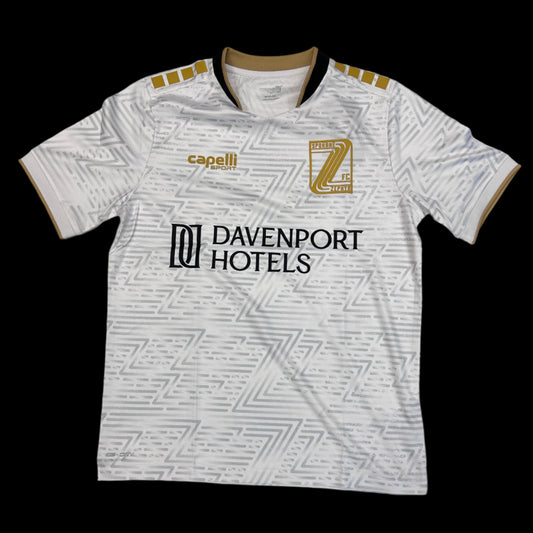 white soccer jersey with a silver repeated "Z" gradient pattern, a black Davenport Hotels logo, a gold Spokane Zephyr "Z" crest and a gold Capelli sport logo