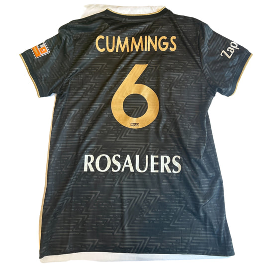 Black sports jersey with 'Cummings 6' and 'Rosauers' printed on it, laid flat on a white surface.